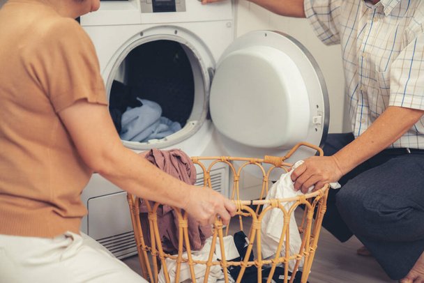 Senior couple working together to complete their household chores at the washing machine in a happy and contented manner. Husband and wife doing the usual tasks in the house. - Foto, Imagem