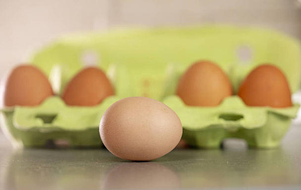 Крупный план простого светлого яйца лежит рядом с коричневыми яйцами в светло-зеленом контейнере. Подготовка к празднику - Фото, изображение