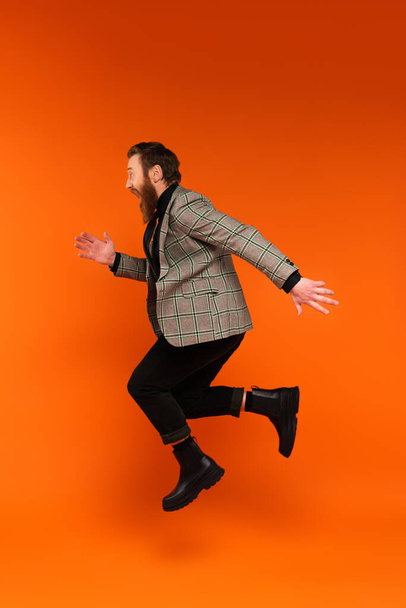 Side view of excited stylish man jumping on red background  - Foto, imagen