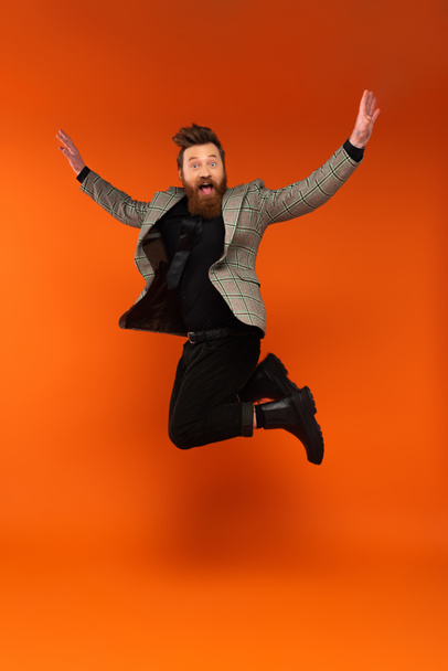 Amazed bearded man in plaid jacket jumping on red background  - Foto, Imagen