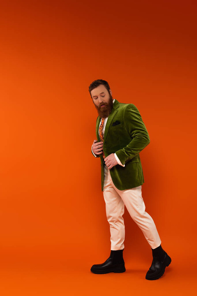 Trendy άνθρωπος σε πράσινο βελούδινο σακάκι με τα πόδια σε κόκκινο φόντο  - Φωτογραφία, εικόνα