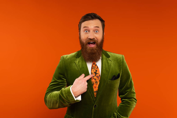 Excited bearded model in jacket pointing with finger at himself on red background  - 写真・画像