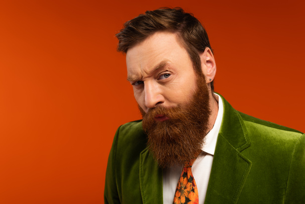 Focused bearded man in green blazer looking at camera on red background  - Foto, immagini