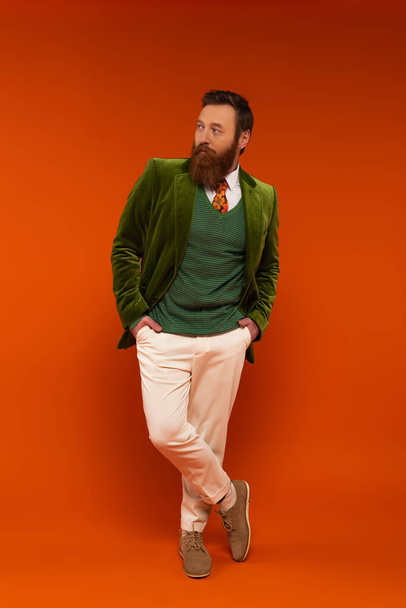 Uomo barbuto alla moda che si tiene per mano in tasche di pantaloni su sfondo rosso  - Foto, immagini
