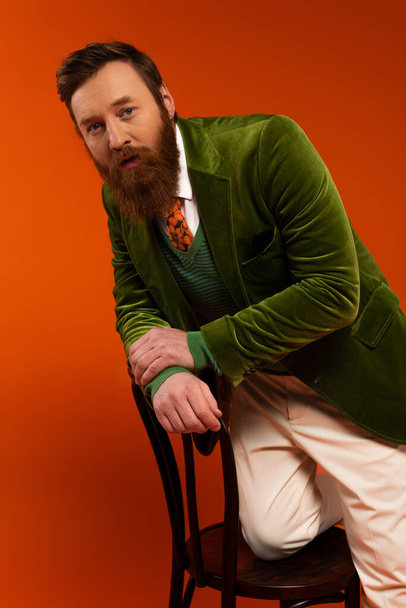 Fashionable bearded model posing on wooden chair on red background  - Fotografie, Obrázek