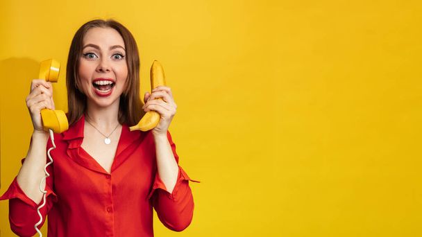 Vtipná tvář s banánem a telefonním sluchátkem. Mladá žena s úsměvem drží v ruce banán. Vtipné výrazy. Koncept výživy. Žlutý styl. Vitamíny. Prázdné místo pro text nebo - Fotografie, Obrázek