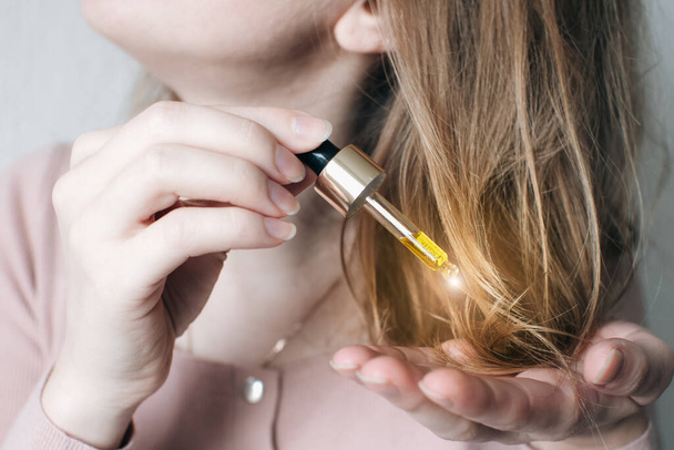 Cosmetic oil for hair in a pipette. Beauty, medicine and  health care concept. Liquid drop dripping on woman hair. Treatment of baldness.Hair growth problems.  Alopecia area on head. - 写真・画像