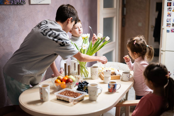 Children eat fruits and desserts, drink tea at home in the evening kitchen. - Foto, imagen