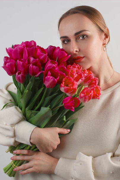 Verticale studio shot van jonge blanke vrouw met boeket van rode tulpen. - Foto, afbeelding