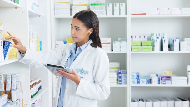 A young female pharmacist stocktaking in a dispensary using a tablet. Doctor preparing prescriptions and medication at clinic or pharmacy. Healthcare professional sorting medicine with digital device. - Photo, Image
