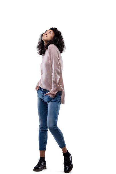 Mladá žena v džínách a růžovém svetru, portrét krásné módní modelky s kudrnatými vlasy pózující. Izolováno na průhledné nebo bílé. - Fotografie, Obrázek