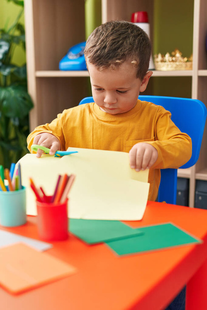 Schattige blanke jongen student snijden papier zitten op tafel op de kleuterschool - Foto, afbeelding