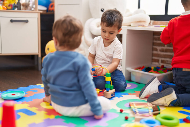 Группа детей, играющих с игрушками, сидящих на полу в детском саду - Фото, изображение