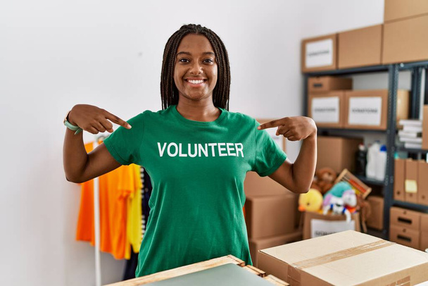 jonge afrikaanse amerikaanse vrouw wijzend met vingers naar vrijwilliger uniform op liefdadigheidscentrum - Foto, afbeelding