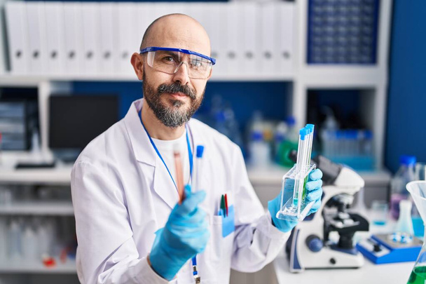 Jeune homme chauve scientifique tenant des éprouvettes en laboratoire - Photo, image