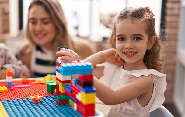 Teacher and toddler playing with construction blocks sitting on table at kindergarten - Foto, imagen