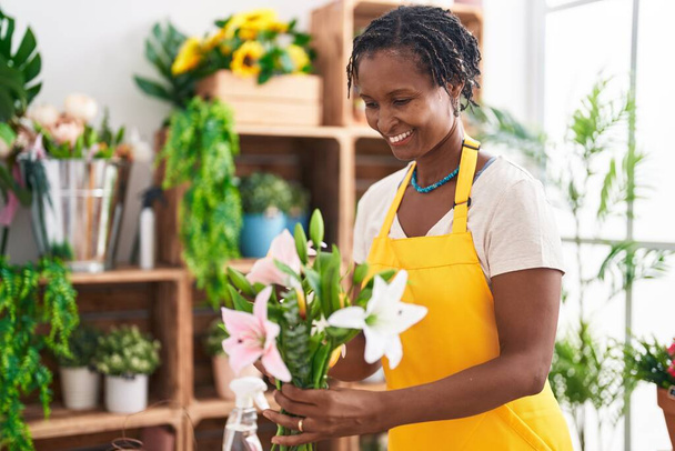 Middle age african american woman florist holding bouquet of flowers at flower shop - Foto, Imagem