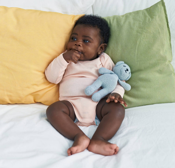 African american baby sitting on bed sucking hand at bedroom - Foto, afbeelding