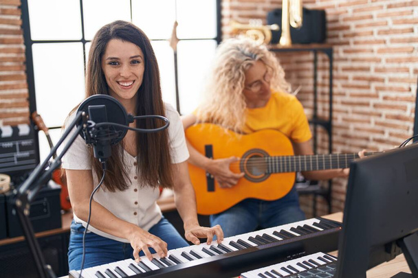 Две женщины-музыкантки поют песни на классической гитаре и фортепиано в музыкальной студии - Фото, изображение