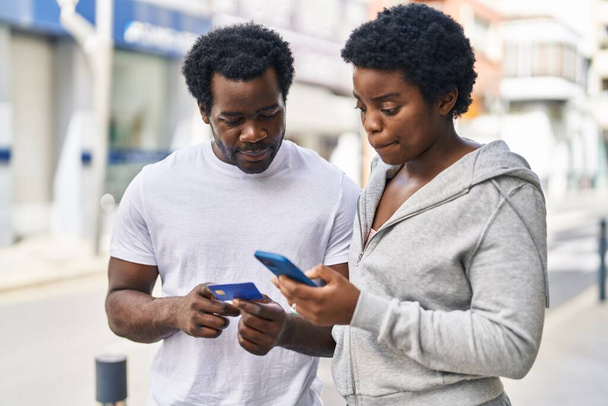 Afrika kökenli Amerikalı erkek ve kadın çift sokakta akıllı telefon ve kredi kartı kullanıyor. - Fotoğraf, Görsel