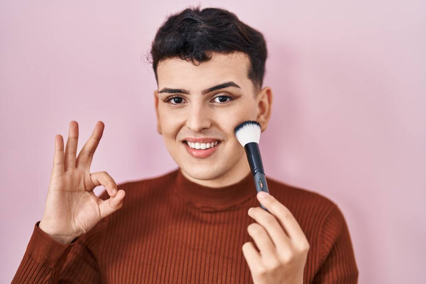 Non binary person applying make up doing ok sign with fingers, smiling friendly gesturing excellent symbol  - Photo, Image