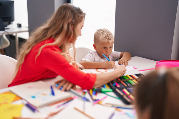 Öğretmen ve yeni yürümeye başlayan çocuk sınıfta masaya oturmuş kağıda resim çiziyorlar. - Fotoğraf, Görsel