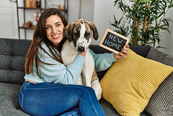 Giovane donna in possesso di nuova lavagna casa abbracciare cane seduto sul divano a casa - Foto, immagini