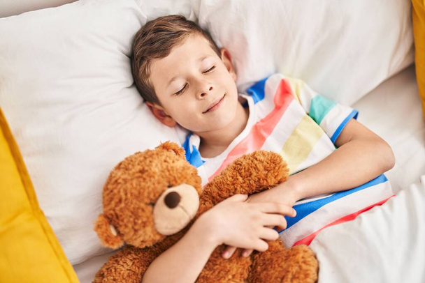 Ξανθό παιδί αγκαλιάζει αρκουδάκι κοιμάται στο κρεβάτι στο υπνοδωμάτιο - Φωτογραφία, εικόνα
