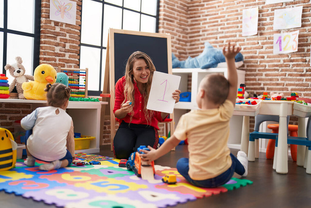 Professor com menino e menina sentados no chão tendo aula de matemática no jardim de infância - Foto, Imagem