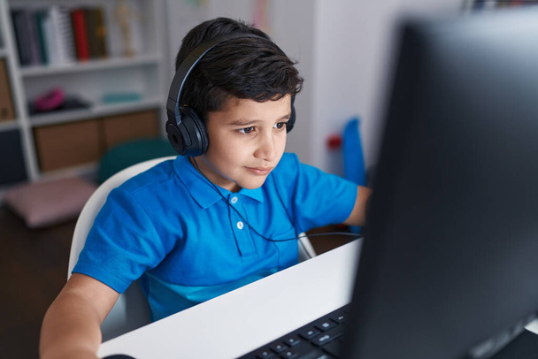 Adorable hispanic boy student using computer sitting on table at classroom - Photo, image