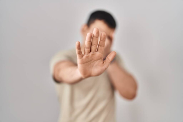 Молодой араб в обычной футболке закрывает глаза руками и делает остановку жеста с грустным и испуганным выражением лица. смущенная и негативная концепция.  - Фото, изображение