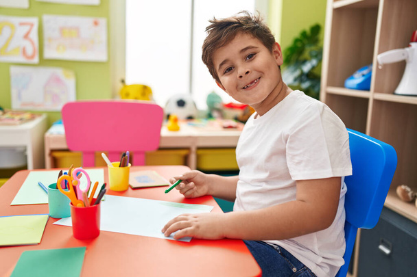 Симпатичный латиноамериканец-дошкольник сидит за столом и рисует на бумаге в детском саду. - Фото, изображение