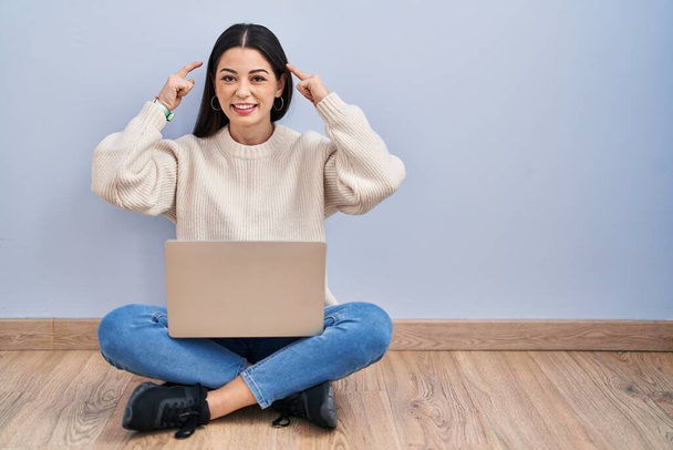 Fiatal nő használ laptop ül a padlón otthon mosolygós mutató fej két kézzel ujját, nagy ötlet vagy gondolat, jó memória  - Fotó, kép