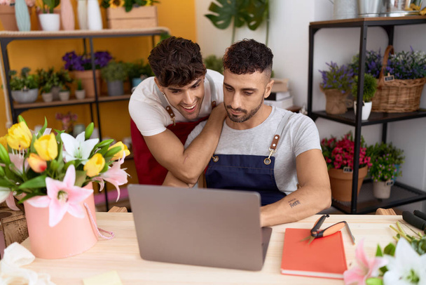 Two hispanic men florists smiling confident using laptop working at flower shop - Foto, Bild