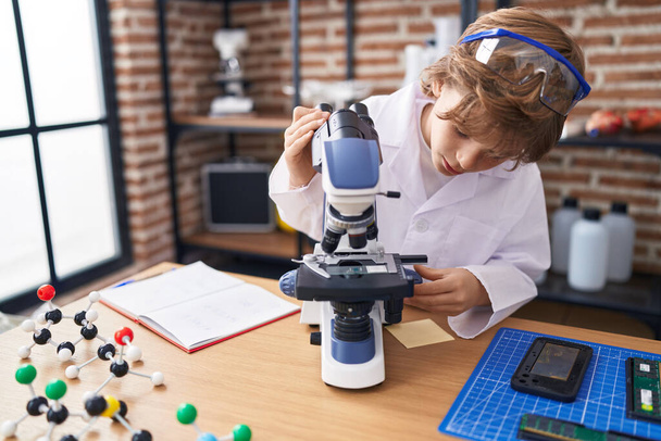 Imádnivaló kaukázusi fiú diák mikroszkóppal az osztályteremben - Fotó, kép