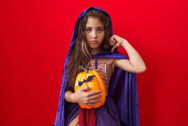 Petite fille hispanique portant un costume de sorcière d'Halloween avec un visage en colère, signe négatif déplaisant avec les pouces baissés, concept de rejet  - Photo, image