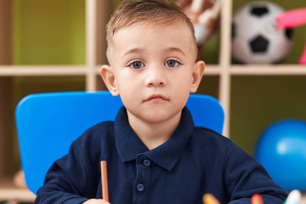 Adorable hispanic boy preschool student sitting on table drawing on paper at kindergarten - Fotó, kép