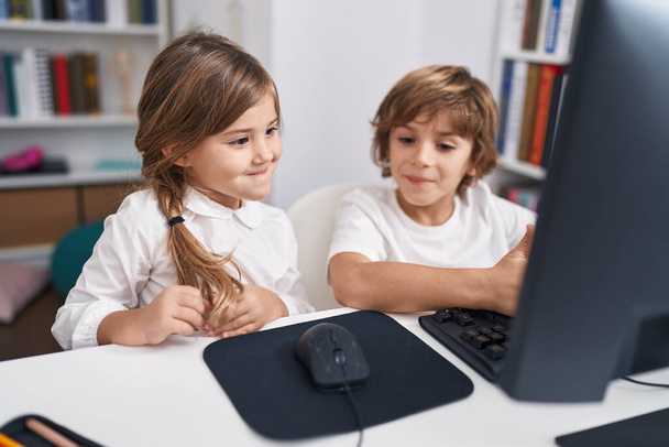 Brother and sister students using computer sitting on table at classroom - 写真・画像
