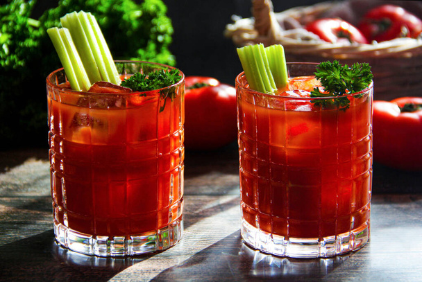 tomato juice close up with fresh tomatoes and basil on a dark background. two glasses of bloody mary cocktail with fresh celery and parsley on a wooden table in natural lightning, rustic style. Fresh vegetable juice with tomatoes - Fotoğraf, Görsel