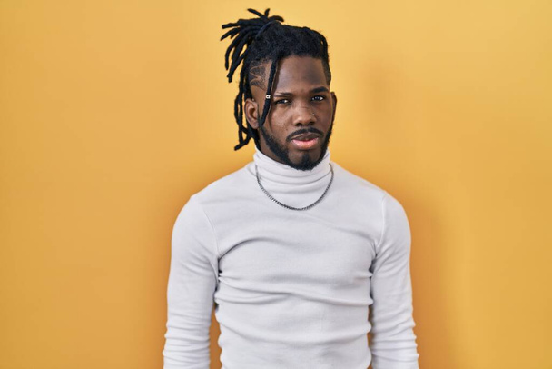 African man with dreadlocks wearing turtleneck sweater over yellow background skeptic and nervous, frowning upset because of problem. negative person.  - Valokuva, kuva