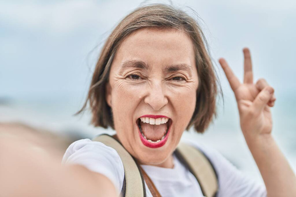 Middle age woman smiling confident making selfie by camera at seaside - Photo, Image