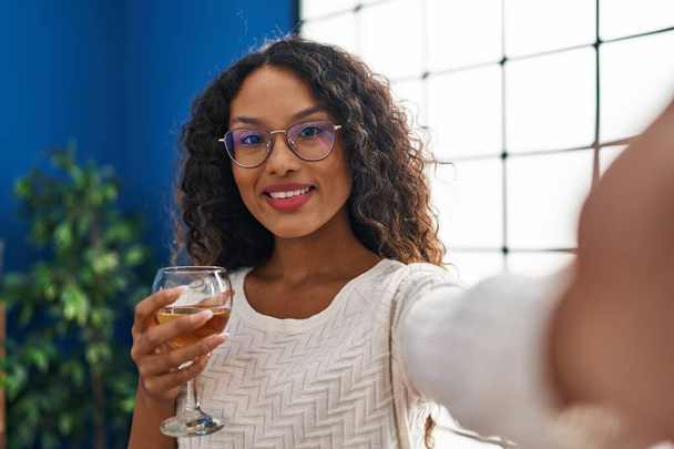 Young latin woman drinking champagne making selfie by the camera at home - Photo, Image