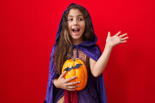 Маленька іспаномовна дівчинка в костюмі відьми Хеллоуїн святкує перемогу з щасливою посмішкою і виразом переможця з піднятими руками
  - Фото, зображення