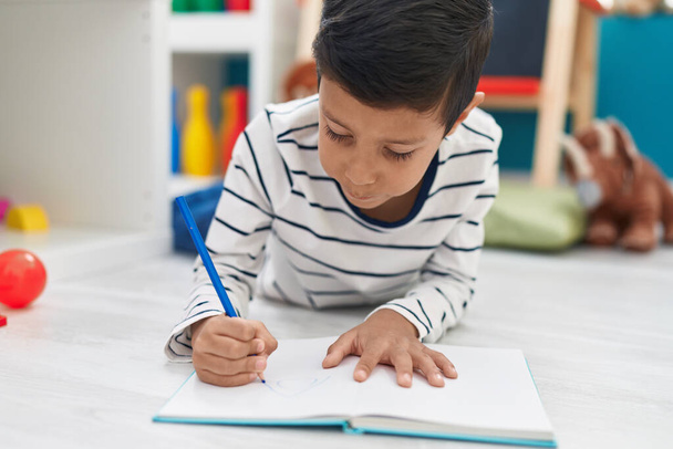 Adorable estudiante hispano escribiendo en un cuaderno en el jardín de infantes - Foto, Imagen