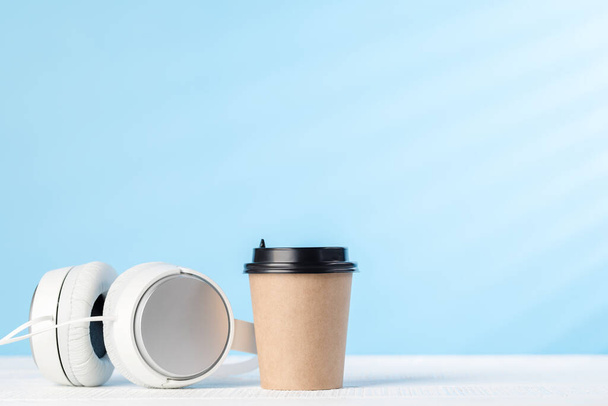 White headphones and coffee cup on blue background with copy space - Foto, imagen