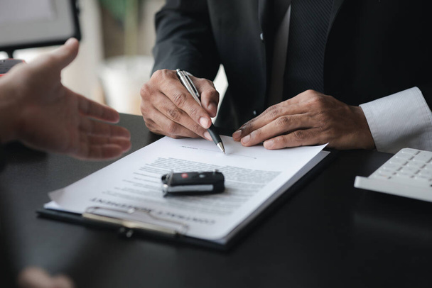 A car rental company employee pointed out the renter to sign the rental agreement after discussing the details and rental terms with the renter. Concept of car rental. - Photo, Image