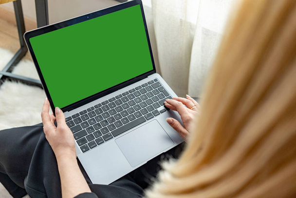 Una joven sostiene un ordenador portátil que mira una maqueta de una pantalla de ordenador verde en línea entrenamiento de PC. Vista de cerca sobre el hombro. Foto de alta calidad - Foto, imagen