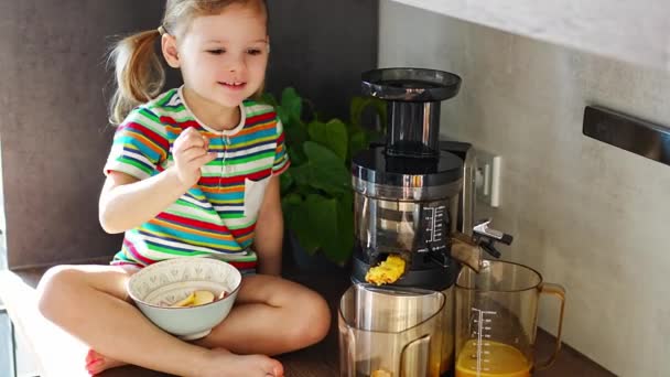 Маленькая девочка делает свежий сок сидя на столе в домашней кухне. Высококачественные 4k кадры - Кадры, видео