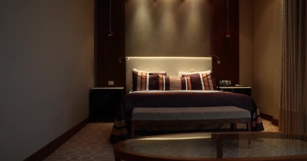Όμορφο κομψό δωμάτιο ξενοδοχείου με κρεβάτι στο εσωτερικό βράδυ. Κρεβατοκάμαρα σε αποχρώσεις του καφέ - Πλάνα, βίντεο