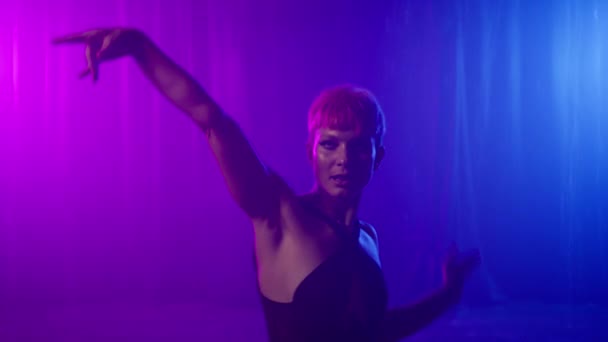 Gorgeous girl poses in studio, emotionally looking at camera. Portrait of beautiful young woman dancing in illuminated by colorful blue purple and pink neon lights. Fashion model slow motion on RED - Felvétel, videó